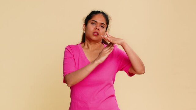Indian woman creates timeout gesture with hands, looking intently at camera needing short pause. Girl on beige background clearly signaling need for break, rest or temporary halt, requiring attention