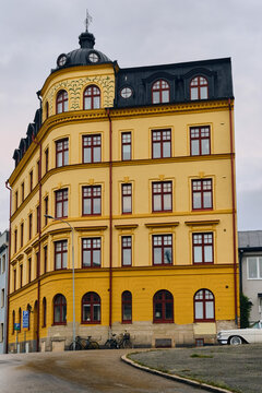 Karlskrona, Sweden - 14 September 2025: View of a yellow classical residency building with a black mansard roof and a small dome on a steep street corner.