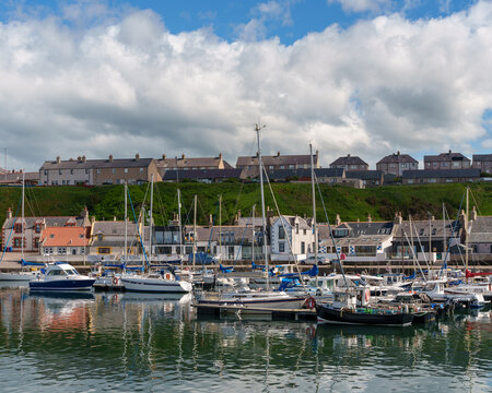 Boats moored in Findochty harbor under a cloudy sky, with houses lining the waterfront and hillside in Moray, Scotland