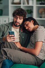 Obraz premium Young couple relaxing at home watching smartphone together, sharing social media content and digital connection