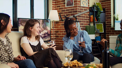 Culturally inclusive group of women talking, drinking wine at reunion gathering, gossiping about...