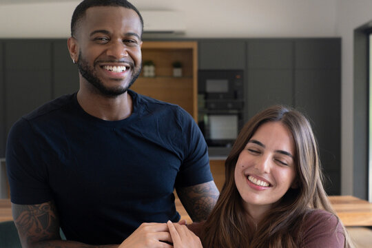 Happy interracial couple smiling and holding hands at home in a modern kitchen, enjoying a tender moment of love, connection and togetherness