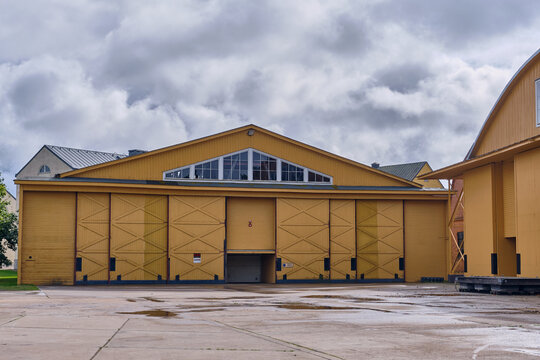 Karlskrona, Sweden - 16 September 2025: View of the historic wooden hangar on Stumholmen island in the naval port, featuring large yellow doors and a triangular window under a cloudy sky.