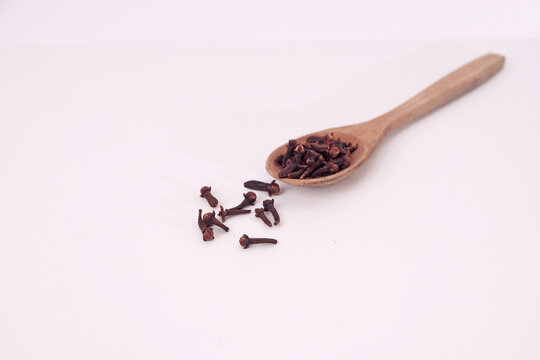 Wooden spoon holds dried cloves. Few cloves rest beside it. Pure white background shows contrast. Simple, clean, and natural composition. Ideal for culinary, herbal, or spice themes