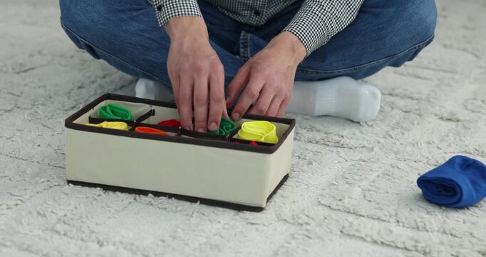 Man putting socks into organizer on floor at home, closeup