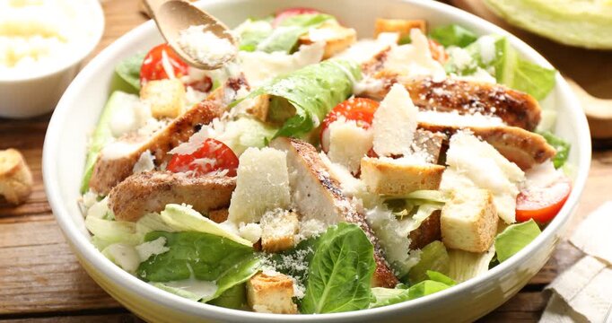 Woman adding cheese to Caesar salad at wooden table, closeup
