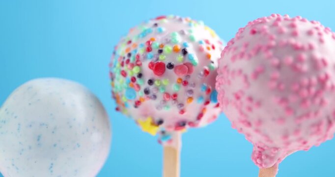 Tasty cake pops on light blue background, closeup. Camera moving left