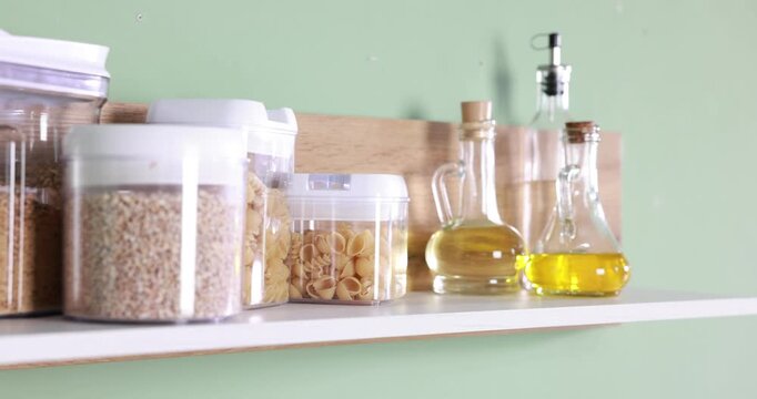 Food products and cooking oils on shelf near green wall indoors, closeup. Camera moving right