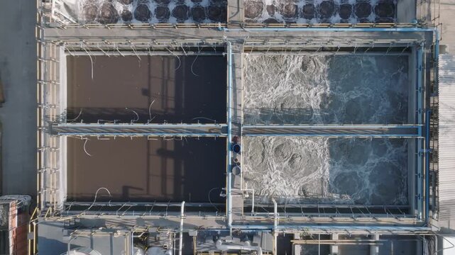 Water recycling plant facility showing rectangular treatment basins with active aeration and settling tanks. Drone shot shows the symmetrical industrial infrastructure and purification process.