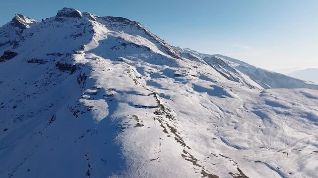 Rohtang Pass mountains display fresh snow coverage with exposed rock outcrops creating contrast against white slopes. Clear blue sky frames the high-altitude Himalayan terrain near Manali in winter.