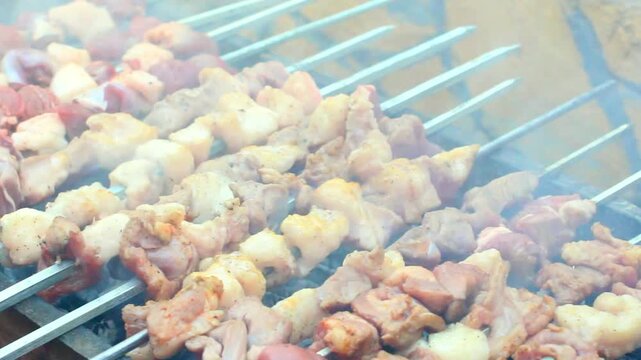 Rows of seasoned meat skewers cooking over hot charcoal smoke at a vibrant outdoor barbecue.