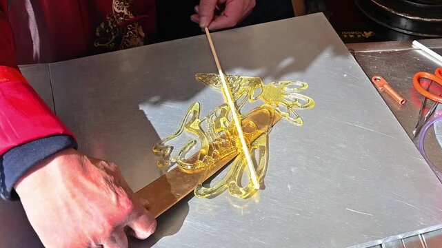 Close-up of elderly Chinese master's hands making traditional sugar painting of a rabbit holding carrot on marble slab