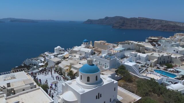 A sweeping high-angle view displays the densely packed, iconic whitewashed village of Oia built along the rugged volcanic cliffs of Santorini, Greece. 