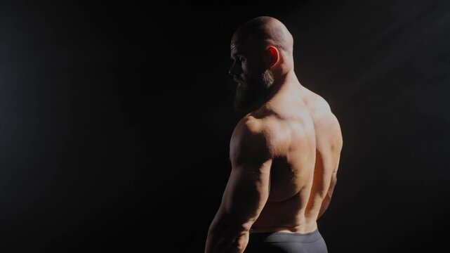 A male bodybuilder poses in shorts, showing off his back muscles.