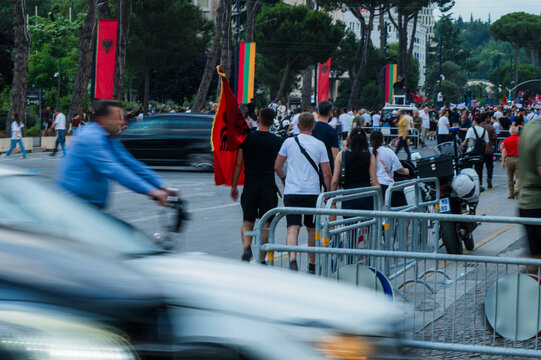 Tirane, Albania - 03 June 2026: View of a crowd of protesters gathering on a city street with Albanian flags and metal barriers under a line of trees.