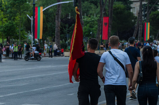 Tirana, Albania - 03 June 2026: View of people walking along a city street during a protest with a man carrying a large Albanian flag and banners hanging in the background.
