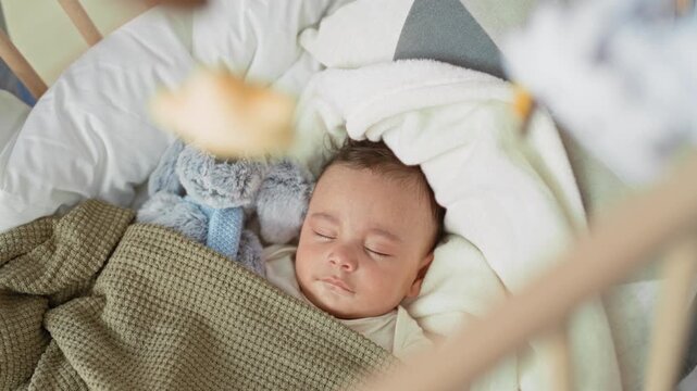 Hispanic baby sleeping with closed eyes and blanket, stuffed toy visible in crib inside building; calm rest.