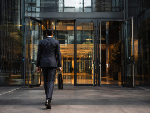 Businessman Walking with a Briefcase Towards a Modern Office Building Entrance