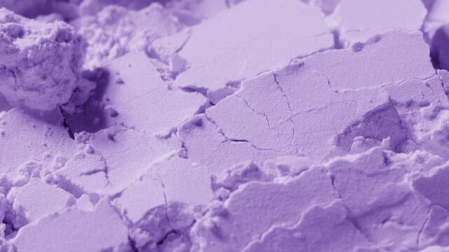 Slow-motion extreme close-up of broken violet powder surface being blown with a strong air stream, chipping it into small pieces
