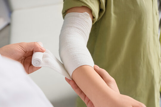 Medical professional applying white elastic bandage to childs injured arm, first aid and injury treatment