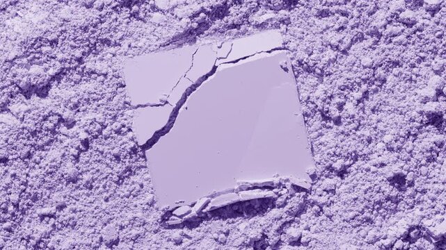 Top view capture of cracked square pressed powder on a violet natural powder surface highlighted by orbiting directional light throwing shifting shadows