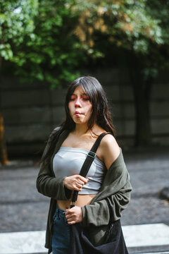 Young Hispanic woman making a playful kissy face with eyes closed in a park to the camera