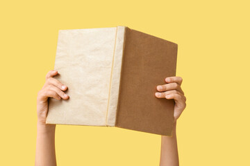 Naklejka premium Hand of little girl holding open book on yellow background