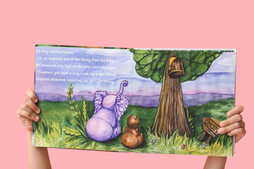 Naklejka premium Hands of little girl holding open fairy tale book on pink background