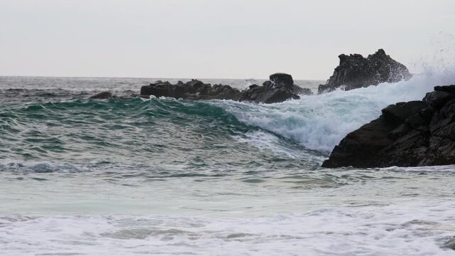 Powerful wave breaking beside rocky coastal outcrops near the shoreline