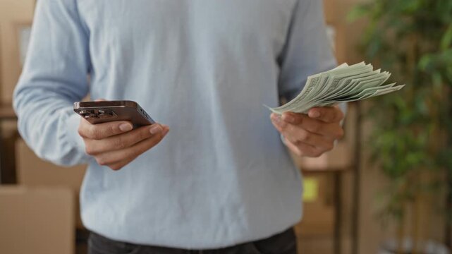 Man holding stack of dollars and smartphone, thumb tapping screen in building; entrepreneurial confidence.