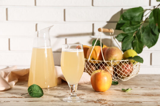 Glass and jug of fresh apple kvass on white wooden table