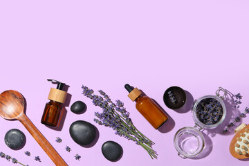 Obraz premium Bottles of lavender essential oil, flowers and spa stones on lilac background