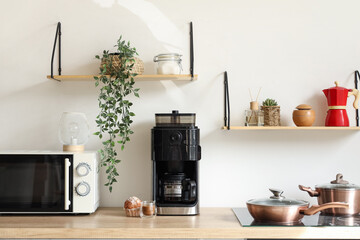 Modern coffee machine with cup of cappuccino and cupcake on table in kitchen