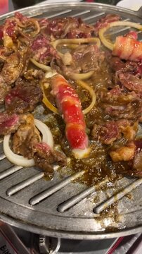 Close up footage of cooking sliced beef marinade with onions on a hot stainless steel grilling pan at a Korean BBQ restaurant. Delicious sizzling meat culinary video commercial mockup.