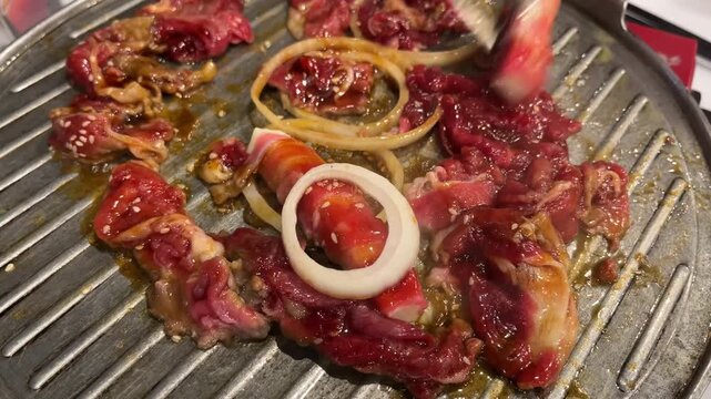 Close up footage of cooking sliced beef marinade with onions on a hot stainless steel grilling pan at a Korean BBQ restaurant. Delicious sizzling meat culinary video commercial mockup.