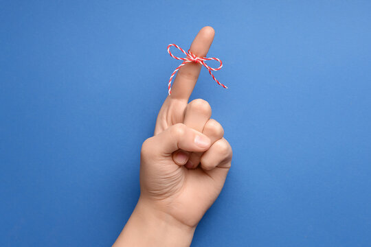 Female hand with red bow on index finger against blue background. Reminder concept