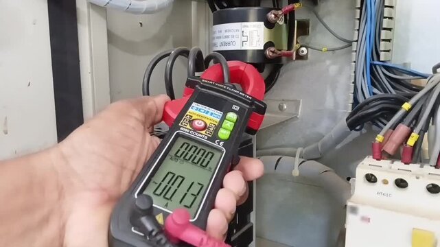 Electrician measuring low neutral current 0.16A using clamp meter to verify perfect phase balance on industrial MCCB breaker panel

