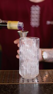 Vertical video. Mixologist work. Making cocktail. Bartender pouring sweet aroma color syrup from metal jigger to glass. Flavored refreshing drink.
