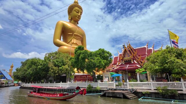 The large golden Buddha at Wat Pak Nam Phasi Charoen is the largest seated Buddha statue in Bangkok, Thailand with Traditional wooden boats in the canals.