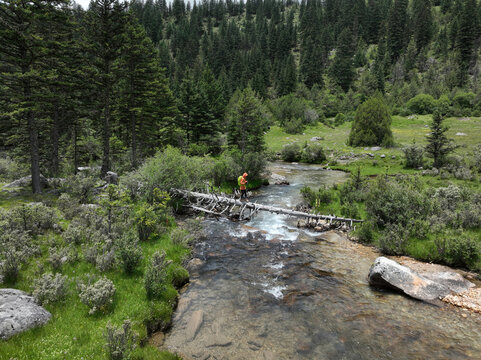 Backpacker walking on one log bridge across the high altitude mountain stream, crossing the river.