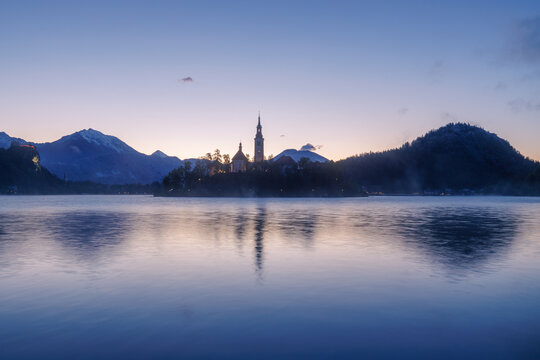 View of the silhouette of the Pilgrimage Church of the Assumption of Mary on Bled Island reflected in the calm waters of Lake Bled at dawn Bled, Radovljica, Slovenia.
