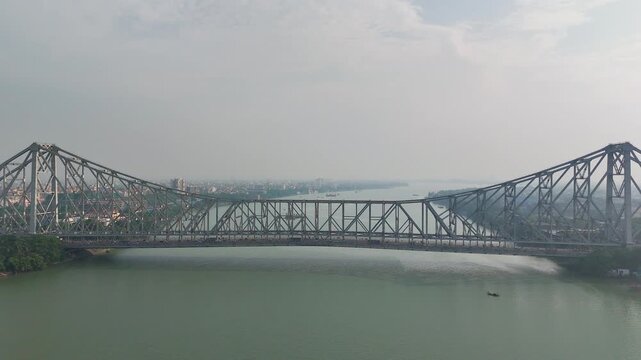A spectacular aerial drone perspective of the historic Howrah Bridge (Rabindra Setu) spanning the Hooghly River, showcasing the iconic cantilever engineering marvel of West Bengal, India.