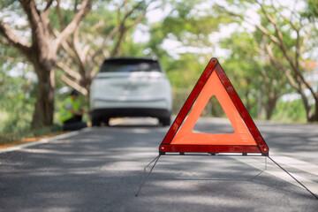 Car breaks down on a quiet road and a person inspects the vehicle with a warning triangle visible in the background © 2B