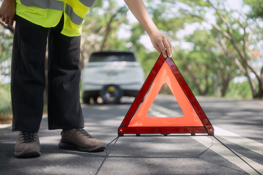 Person places warning sign on road after car issue in rural area during day