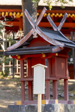 View of a small traditional red Shinto shrine with a distinctive V-shaped roof and a wooden sign in Nara, Nara, Japan.