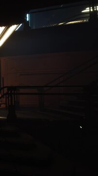 A train station is shown at night with dim lighting. The scene includes a staircase and a dark platform. Overhead lights create a moody atmosphere in the area.