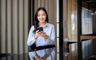 Fototapeta premium Young businesswoman smiling while using smartphone during a coffee break in a modern cafe workspace.