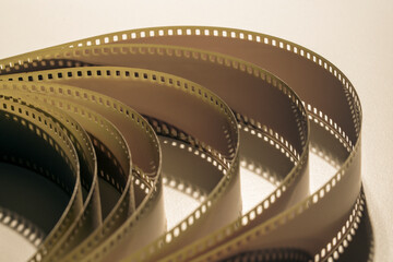 Naklejka premium Vintage 35mm film strip rolls texture background, closeup. Macro shot of tangled celluloid 35mm film strip with perforated holes on light background cinema concept
