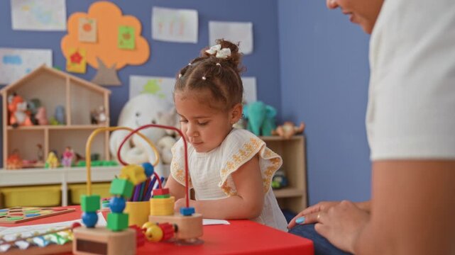 Young girl drawing with colored pencil and bead maze toy at red table in preschool building; concentration joy learning.
