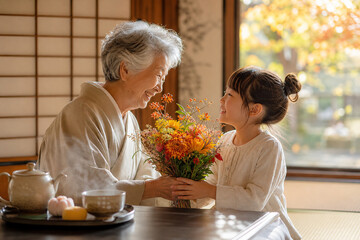 Granddaughter Giving Flowers to Grandmother for Respect for the Aged Day,敬老の日に孫から花束を受け取る祖母の温かな家族写真